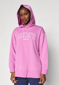 Roosa kapuutsiga pusa, mis on valmistatud pehmest kangast ja millel on suur valge "DKNY" logo ning "NEW YORK" tekst, lõdvestunud lõikega ja nööriga kapuuts.