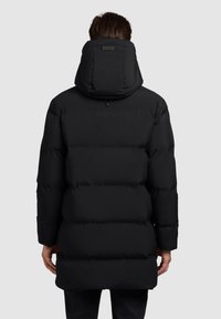 Zwarte pufferjack met hoge kraag en vaste capuchon, gekenmerkt door een gestikt ontwerp, subtiele textuur en een rechte snit.