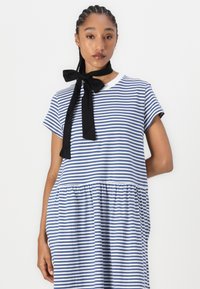 Blau-weiß gestreifter Kleid mit kurzen Ärmeln, einer gerafften Taille und einer schwarzen Schleifenakzent am Ausschnitt. Glatte Baumwollstruktur.