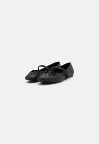Bailarinas negras con un upper texturizado y brillante, puntera redondeada y un lazo como acento, con suela plana y diseño minimalista.