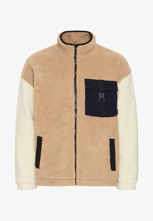 Fleecejakke med en beige krop, hvide ærmer og en marineblå lappe-lomme. Har en lynlås lukning og sorte detaljer. Struktureret og varm.