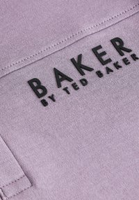 Violetinė medžiaga su lygiu paviršiumi, viduryje esantis išraiškingas juodas tekstas "BAKER" ir mažesnis tekstas "by TED BAKER".