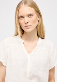 Lettet, tekstureret, off-white bluse med V-hals, korte ærmer og knaplukning, der har diskrete rynkedetaljer.