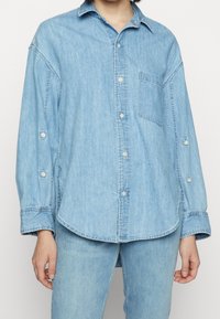 Denim skjorta med knappar i ljusblått, med en bröstficka, lång ärm och en lätt böjd nederkant. Har knappmanchetter och avslappnad passform.