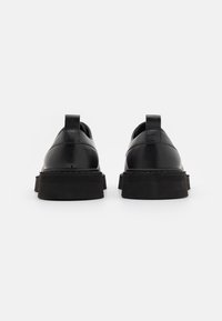Scarpe in pelle nera con finitura liscia, forma arrotondata e suole in gomma nera testurizzata. Dotate di un occhiello sul retro per facilitare l'indossamento.