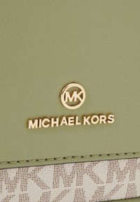 Lysegrøn kunstlæderpung med et guld logo og en creme accents med et gentaget mønster. Glat tekstur med sømdetaljer.