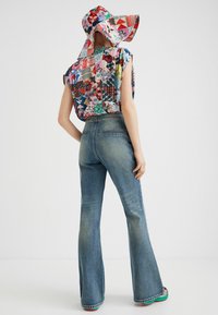 Persona che indossa un top senza maniche a patchwork multicolore e un cappello a tesa larga coordinato, con jeans a vita alta svasati blu e scarpe colorate.