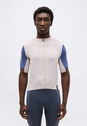 Férfi, bézs és kék színű, testhez simuló, rövid ujjú kerékpáros mezben, elöl cipzárral, és sötétkék bélelt kerékpáros rövidnadrágban.