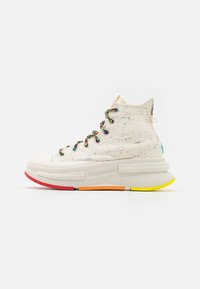 High-top sneakers with a speckled off-white canvas upper and multicolor laces. Features a thick, colorful sole with red, orange, and yellow accents.