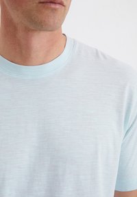 Lichtblauwe T-shirt met korte mouwen en een ronde hals. De textuur is glad met een subtiel gemêleerd patroon.