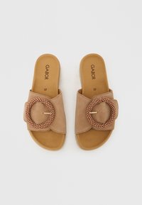 Beige Slide-Sandalen mit einem breiten Riemen, der eine strukturierte runde Schnalle und kreisförmige perlenartige Akzente aufweist. Obermaterial aus weichem Wildleder und gepolsterte Innensohle.