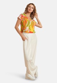 Korte mouwen, v-hals blouse met een kleurrijk bloemenpatroon; gecombineerd met losvallende, licht crèmekleurige broek en witte sneakers.