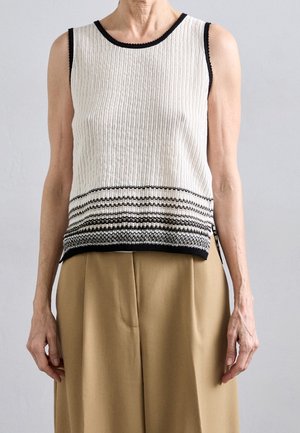 Sleeveless white knit top with black trim and horizontal black stripes near the hem, worn with high-waisted beige pants.