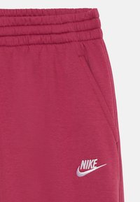 Bordo spalvos sportiniai kelnių su elastine juosta, šoninėmis kišenėmis ir balta siuvinėta Nike logo ant kairiojo šlaunies. Lygus medvilnės paviršius.