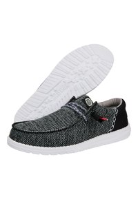 Scarpe slip-on in tessuto nero e grigio con suola in gomma bianca, dotate di una tomaia texture, dettagli intrecciati e un accento rosso a contrasto.