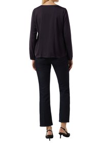 Blouse à manches longues, de couleur violet foncé, avec un col carré, associée à un jean en denim foncé. Des talons noirs à lanières complètent la tenue.