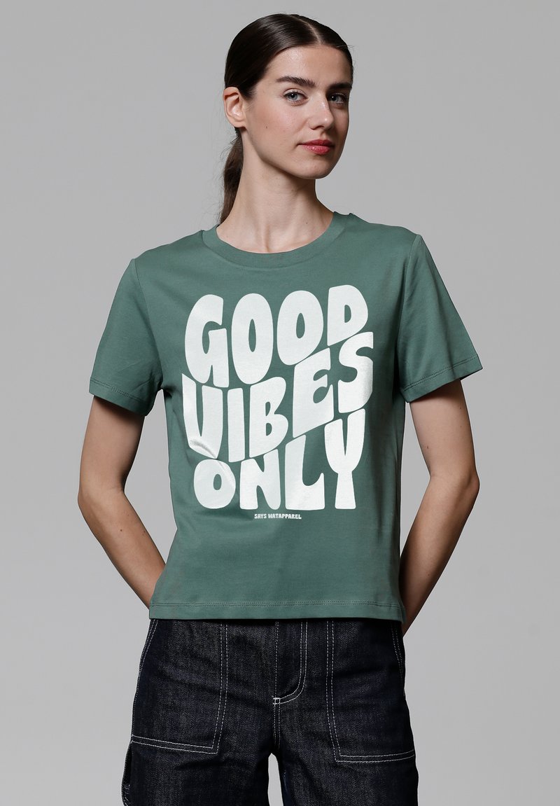 Groene katoenen t-shirt met korte mouwen, voorzien van grote witte tekst "GOOD VIBES ONLY" in een vet, speels lettertype.