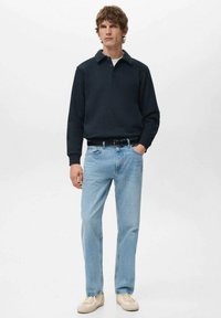 Granatowy pulower z kołnierzykiem, jasnoniebieskie dżinsy i beżowe trampki. Pulower ma miękką fakturę i luźny krój.