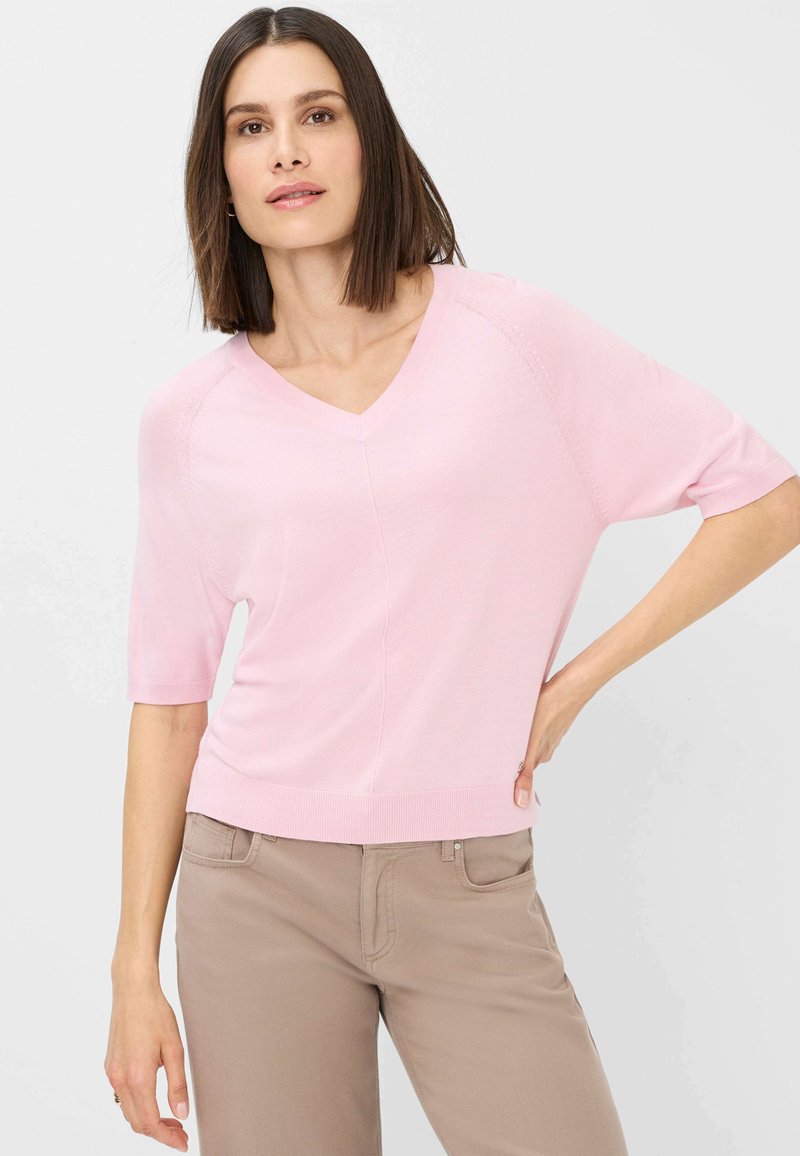 Lyserød T-shirt med korte ærmer og V-udskæring, med en afslappet pasform og ribbede kanter. Tekstureret detalje på ærmerne tilføjer en subtil visuel interesse.