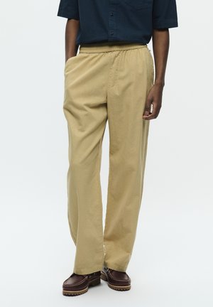 Beige, wide-leg pants with an elastic waistband and side pockets, paired with dark brown shoes featuring a rugged sole.