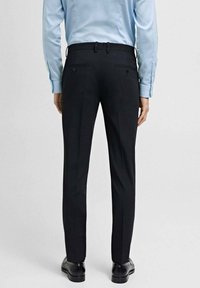 Svart skräddarsydda byxor med slim fit, slät textur och bälteshällor. Har två bakfickor med knappar. Bärs med en ljusblå skjorta.