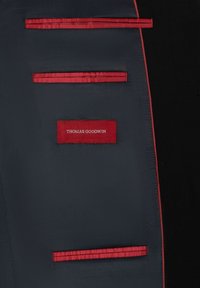 Anzug-Innenleben mit einem navyfarbenen Stoff mit glatter Textur, akzentuiert durch rote gestreifte Taschen und ein rotes Etikett mit weißem Text: "THOMAS GOODWIN."