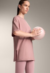 Light pink oversized t-shirt with short sleeves, side slits, and soft texture. Model holding a smooth, round pale pink exercise ball.