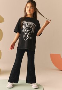Sort oversized T-shirt med Rolling Stones-logo, parret med flagrende lacebukser. Hvide sneakers fuldender outfittet og har et tekstureret, blomsterdesign.