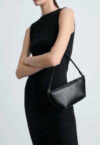 Sac à main en cuir noir avec un design structuré et un fond courbé, doté d'une poignée courte et d'accents en métal argenté.