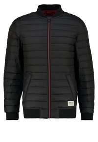 Musta toppatakki, jossa on vetoketjullinen suljin, resorit hihansuuissa ja punainen vuori sisäpuolella. Taskut sivuilla ja etiketti vasemmassa alakulmassa.