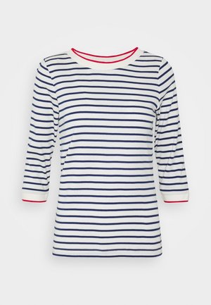 Chemise blanche à manches longues avec des rayures horizontales bleu marine et une bordure rouge au col et aux poignets, présentée sur un fond uni.