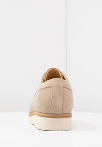 Chaussure en suède beige avec un bout arrondi. Présente une semelle claire contrastante et des coutures visibles le long de l'arrière et des côtés. Design minimaliste.