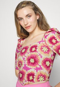 Top floral com mangas curtas bufantes, apresentando um fundo rosa e grandes padrões florais amarelos e verdes. Design cropped com decote quadrado.