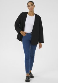 Čierny oversized blejzer s voľným strihom a jediným gombíkom, kombinovaný s priliehavým bielym topom a modrými úzkymi džínsami. Čierne topánky.