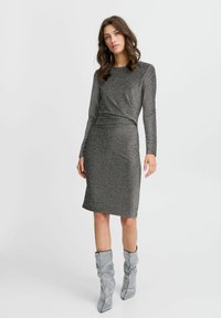 Siva haljina dugih rukava izrađena od metalnog, sjajnog materijala. Uže krojena, do koljena, s elegantnim detaljima šivanja. Uparena s srebrnim, teksturiranim čizmama.