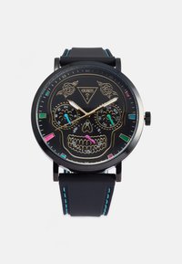 Orologio analogico nero con design di teschio sul quadrante. Presenta dettagli dorati, due sotto-quadranti e un cinturino in gomma con cuciture blu.