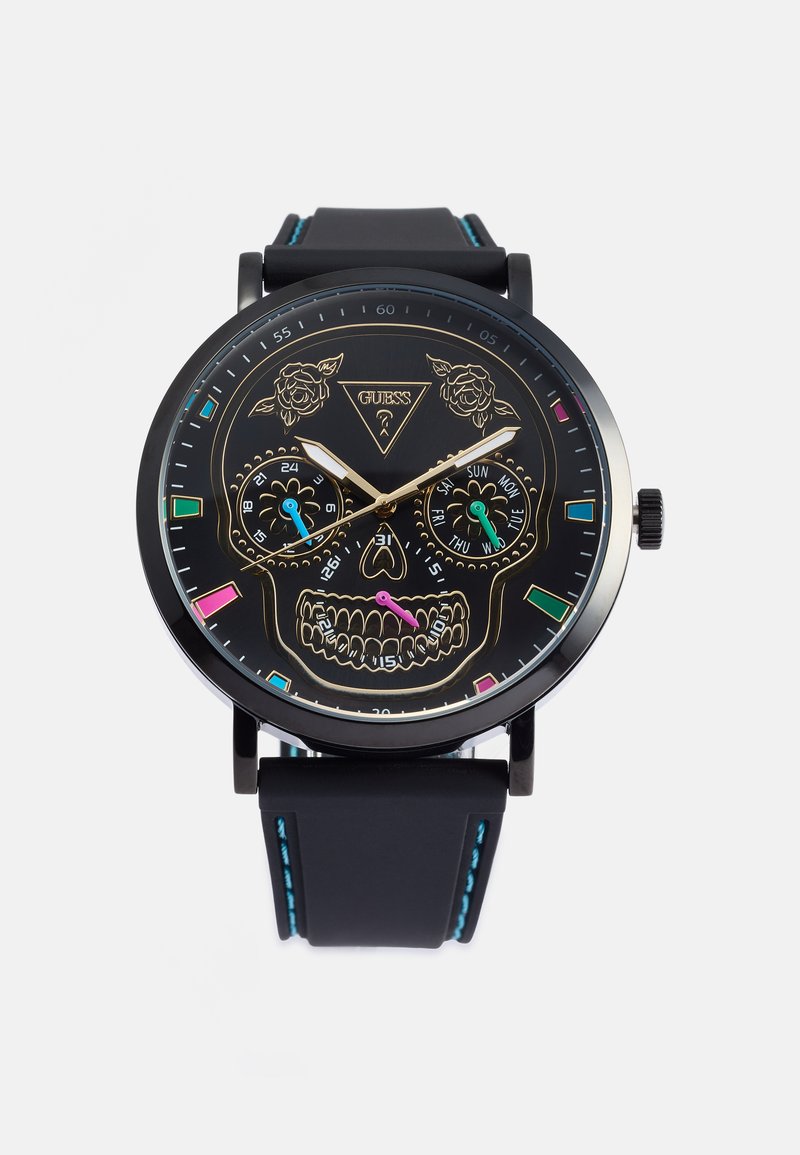 Orologio analogico nero con design di teschio sul quadrante. Presenta dettagli dorati, due sotto-quadranti e un cinturino in gomma con cuciture blu.