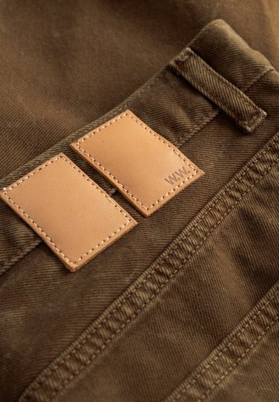 Brown fabric with visible texture, featuring two rectangular leather patches stitched onto it, one embossed with "WWW."