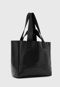 Saco tote preto feito de material brilhante com duas alças longas, lados diretos e um detalhe de bolso retangular na frente.