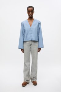 Light blue, cropped blouse with a V-neck and button closure, paired with high-waisted, light gray jeans and brown clogs. Smooth texture.