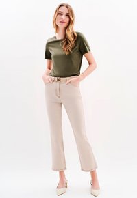Olijfgroene t-shirt met korte mouwen gecombineerd met beige, cropped jeans, met voorzakken en een tankleurige riem met een decoratieve gesp.