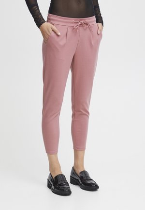 Pantaloni jogger roz, conici, din material moale, având un brâu elastic cu șnur și buzunare laterale. Asortați cu mocasini negri lucioși.