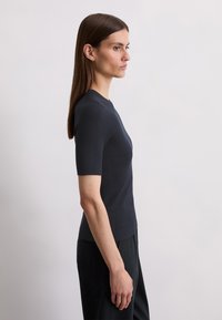 Navy ribbed knit top with short sleeves, round neckline, and a tailored fit, paired with loose dark pants. Smooth texture and subtle detailing.