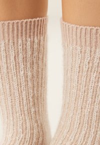 Scaldamuscoli lavorati a maglia in morbido rosa con trama a coste e dettagli scintillanti delicati. Design accogliente che si estende oltre la caviglia.