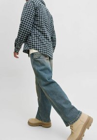 Srajca s dolgimi rokavi v karirastem vzorcu v mornarsko modri in beli barvi, v kombinaciji z dvobarvnimi modrimi kavbojkami in bež čevlji. Poudarek na sproščenem, udobnem kroju in podrobnostih šivanja.