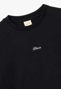 Black cotton t-shirt with a round neckline and short sleeves, featuring white embroidered text "Blkwis" on the front. Soft texture.