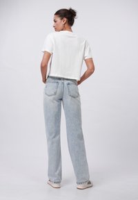 T-shirt blanc cropped à manches courtes, associé à un jean large taille haute bleu clair avec poches arrière et un délavage écoeuré.