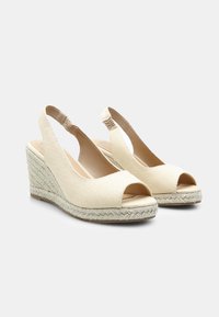 Bež sandale s klinom in odprtim prstom, platnen zgornji del in pletena juta platforma. Imajo elastiko za boljši oprijem in gladek notranji del.