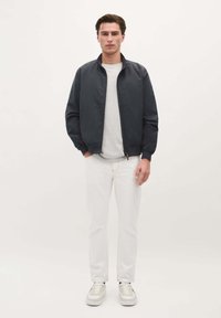 Marinebomberjack met staande kraag, voorkant met rits, witte ronde hals t-shirt, witte slim-fit jeans en lichtgekleurde sneakers.
