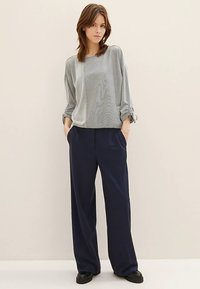 Lichtgrijs, textuurvol longsleeve met opgerolde mouwen, gecombineerd met marineblauwe broek met wijd uitlopende pijpen, voorzien van een gladde afwerking en een ontspannen pasvorm.